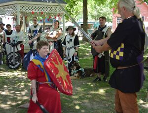 Hubris kneels before Sir Kegg who is holding up a sword to knight him.